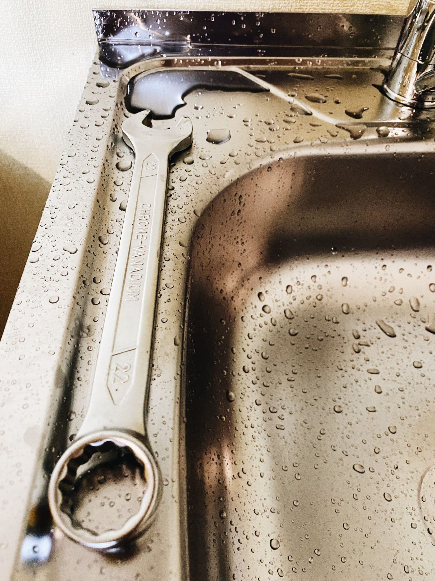 Wrench resting on a wet stainless steel kitchen sink