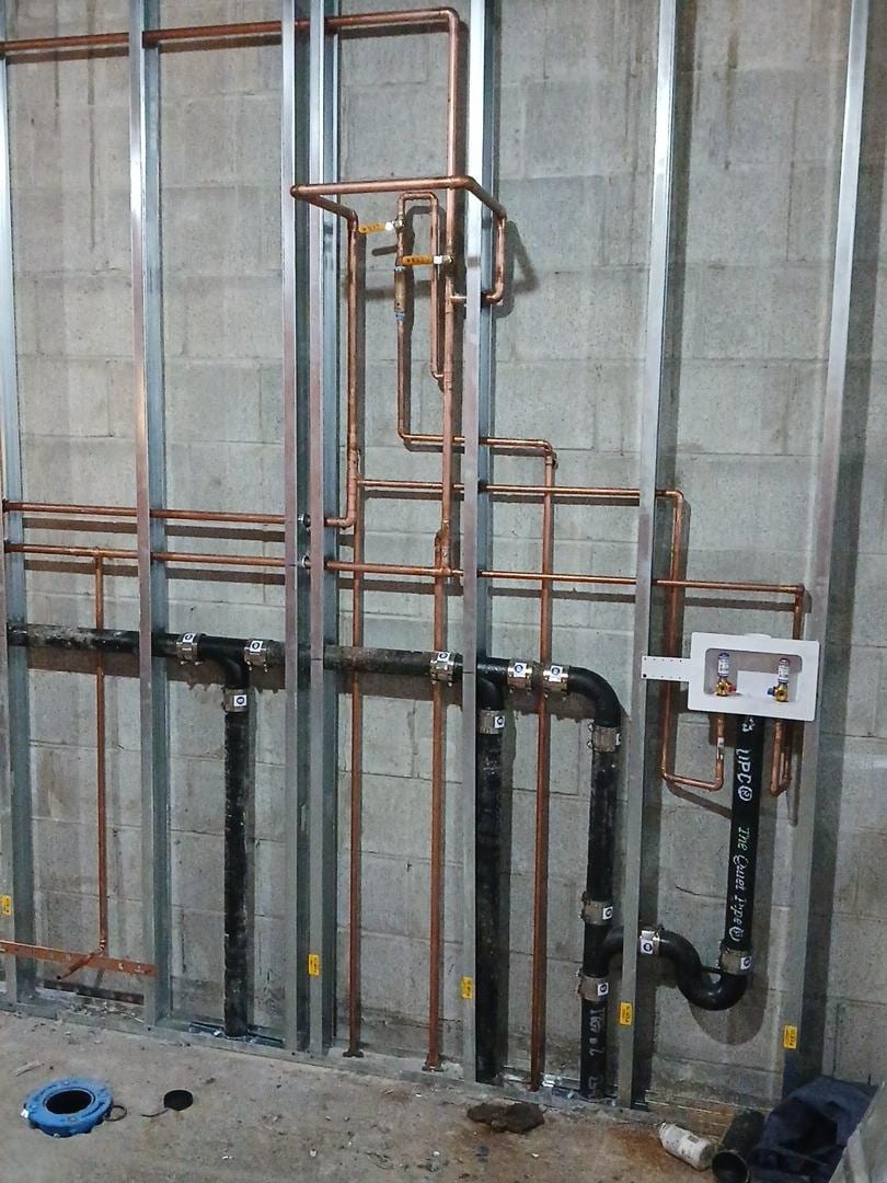 Copper supply lines and black drain piping roughed in for back-to-back bathrooms