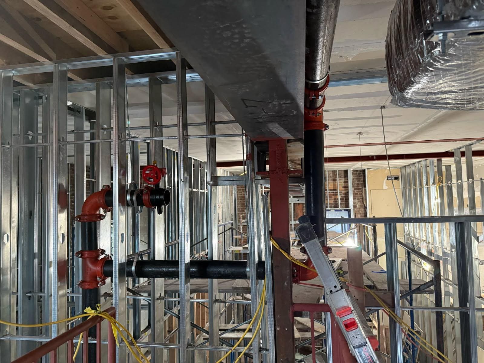 Sprinkler piping with red grooved fittings and a hose valve in a building under renovation