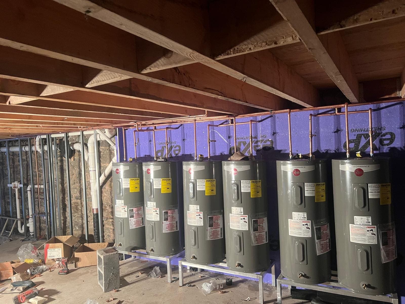 Six electric water heaters connected with new copper piping in a basement